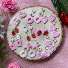 pink and white earrings are arranged on a wood slice with flowers in the foreground