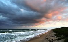 an ocean beach with waves crashing on the shore and clouds in the sky above it