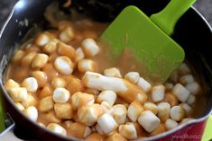 a pot filled with corn and marshmallows next to a green spatula