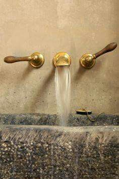 two golden faucets are running water from the wall in this bathroom sink area