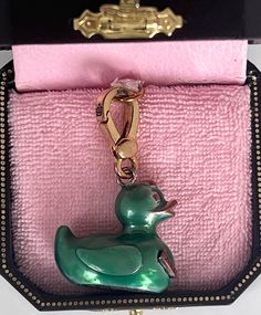 a green rubber duck keychain sitting in a pink velvet case on a white surface