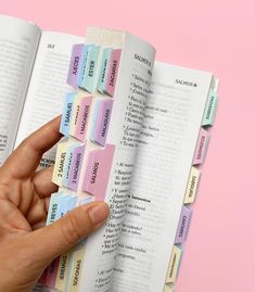 a hand holding an open book with sticky notes attached to it, on top of a pink background