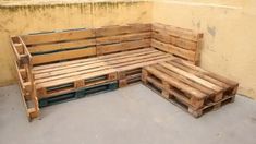 a wooden bench made out of pallets sitting on top of a cement floor next to a yellow wall