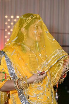 a woman dressed in yellow is looking at her cell phone while wearing a veil and headdress