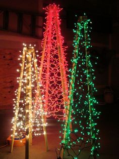 three christmas trees with lights on them in the night time, one is red and one is green