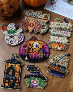 cross stitch halloween ornaments on a table with pumpkins and other items in the background