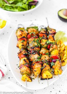 chicken kabobs on skewers with fresh fruit and salad in the background