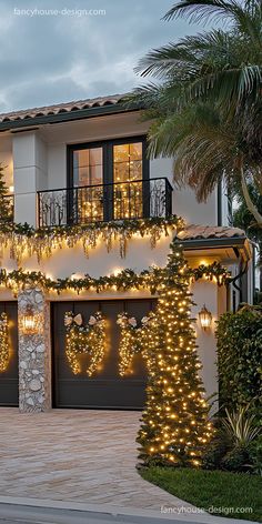 a house decorated for christmas with lights and wreaths on the front door, surrounded by palm trees