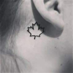 a black and white photo of a woman's ear with a maple leaf tattoo on it