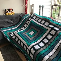 a crocheted blanket is sitting on a couch next to a teddy bear and window