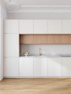 an empty kitchen with white cabinets and wood flooring on the walls, along with wooden floors