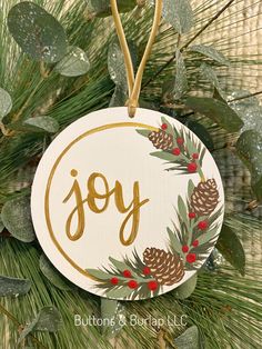 a christmas ornament with the word joy on it hanging from a pine tree