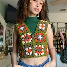 a woman with curly hair wearing a crocheted crop top and jean shorts, standing in a kitchen