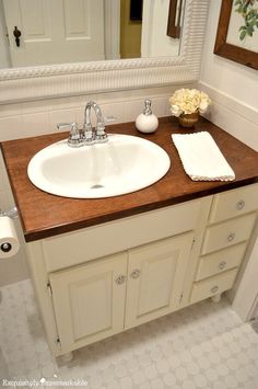 a white sink sitting under a bathroom mirror next to a wooden counter topped with flowers