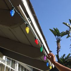 a person is hanging christmas lights on the roof of a house with palm trees in the background