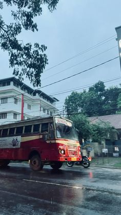 a red and white bus driving down a street next to a tall building on a rainy day