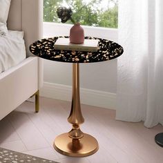 a black and gold table with a pink vase on it in front of a window