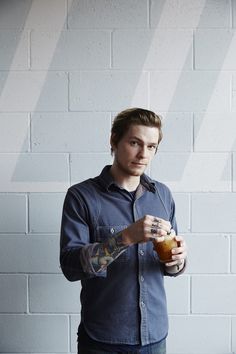 a man holding a drink in front of a white brick wall