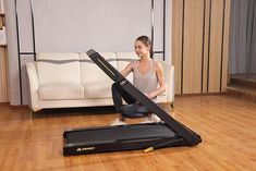 a woman sitting on top of a treadmill in front of a white couch and wooden floor