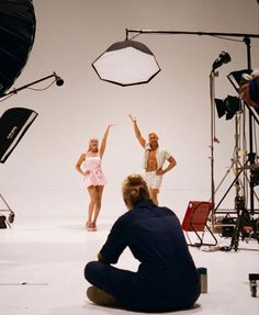 three people are sitting on the ground in front of camera equipment and one person is kneeling down