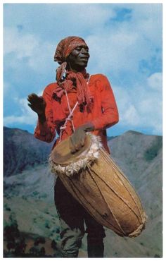 a man holding a large drum on top of a mountain