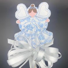 a white angel with blue wings on top of a ribbon and some silver ribbons around it