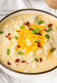 a white bowl filled with cheese and bacon soup on top of a wooden cutting board