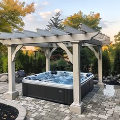 a hot tub sitting under a pergolated covered gazebo next to a stone patio