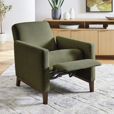 a green chair sitting on top of a rug next to a wooden cabinet and vase