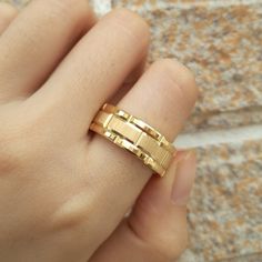 a woman's hand wearing a gold ring that has two bars on it and is next to a brick wall