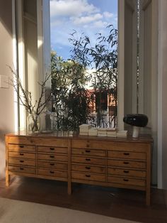 a wooden dresser sitting in front of a window next to a potted bamboo plant