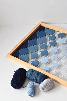 several balls of yarn are sitting in front of a wooden frame on a white surface