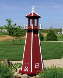 a small red and white lighthouse in the middle of a grassy area next to a road