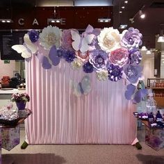 a pink and purple backdrop with paper flowers on it at a wedding reception or event