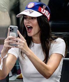 a woman taking a selfie with her cell phone while wearing a hat and white shirt