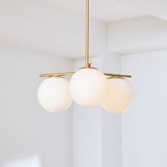 three white balls hanging from a brass chandelier in a room with white walls