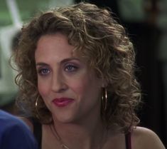 a close up of a woman with curly hair and blue eyes wearing gold hoop earrings