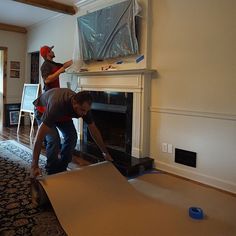 two men working on a fireplace in a living room with carpet and walls being installed