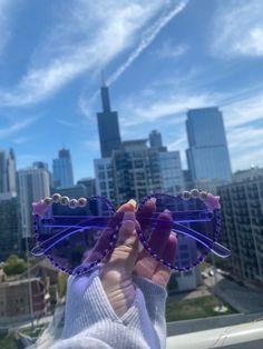 a person holding up a pair of purple sunglasses in front of a cityscape