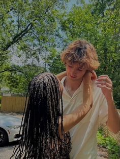 a young man is combing his dreadlocks in front of a parked car