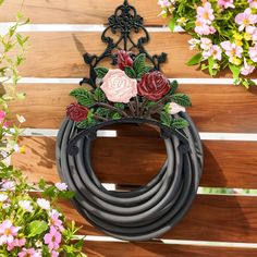 a wreath with flowers hanging on the side of a wooden fence next to pink and white flowers