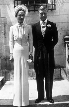 an old black and white photo of two people in formal wear standing on steps with one holding the other's hand