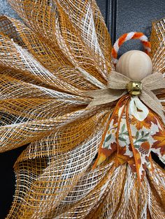 an orange and white mesh wreath with a wooden ball on the top is hanging from a black door