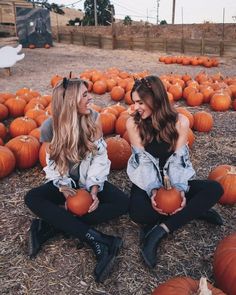 two women sitting on the ground surrounded by pumpkins