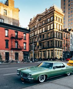 an old green car parked on the side of the road in front of some buildings