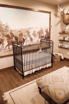 a baby crib in front of a large painting with cowboys on the wall behind it