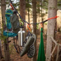 a pair of running shoes hanging from a line in the woods next to a backpack and water bottle