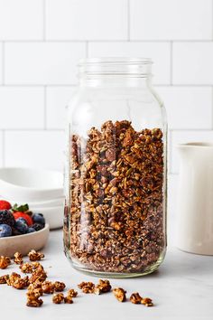 a glass jar filled with granola next to berries