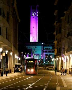 a red bus driving down a street next to tall buildings with a clock tower in the background