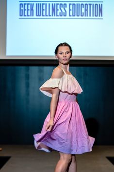 a woman walking down a runway wearing a dress with an off the shoulder top and purple skirt